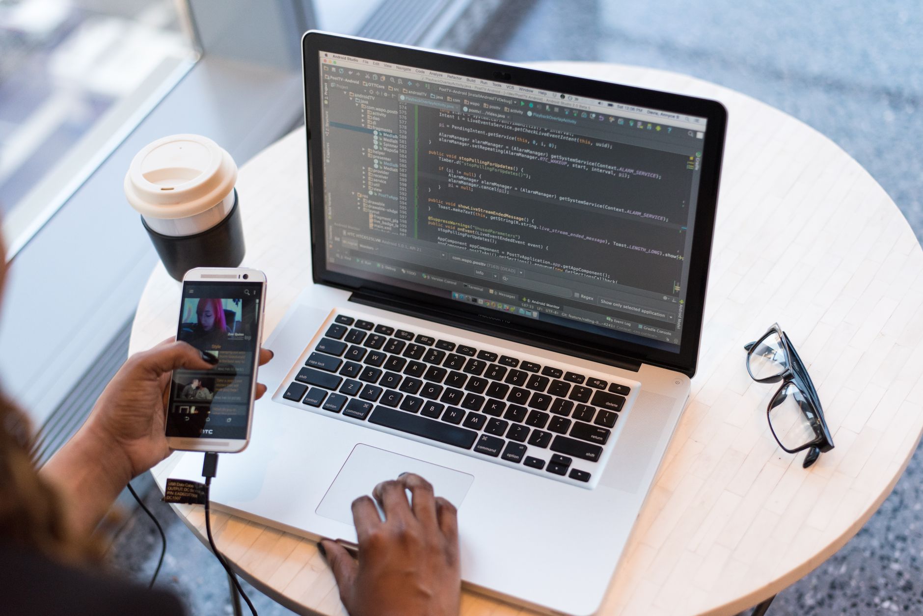 Un programmeur gère du code sur un ordinateur portable tout en effectuant plusieurs tâches avec un smartphone, illustrant l'espace de travail technologique moderne.