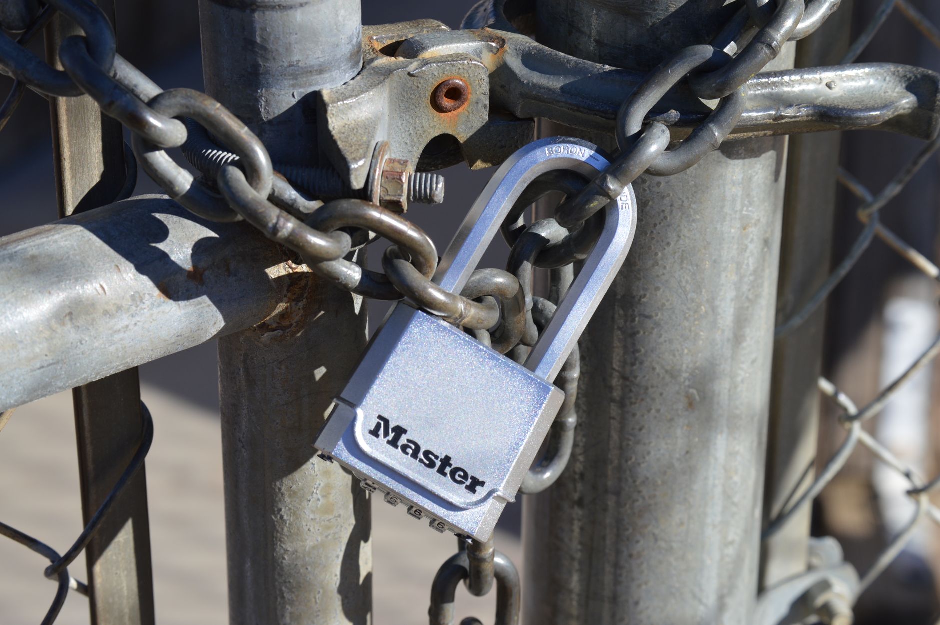 Cadenas à combinaison argenté fermé sur une chaîne qui verrouille un portail métallique grillagé.