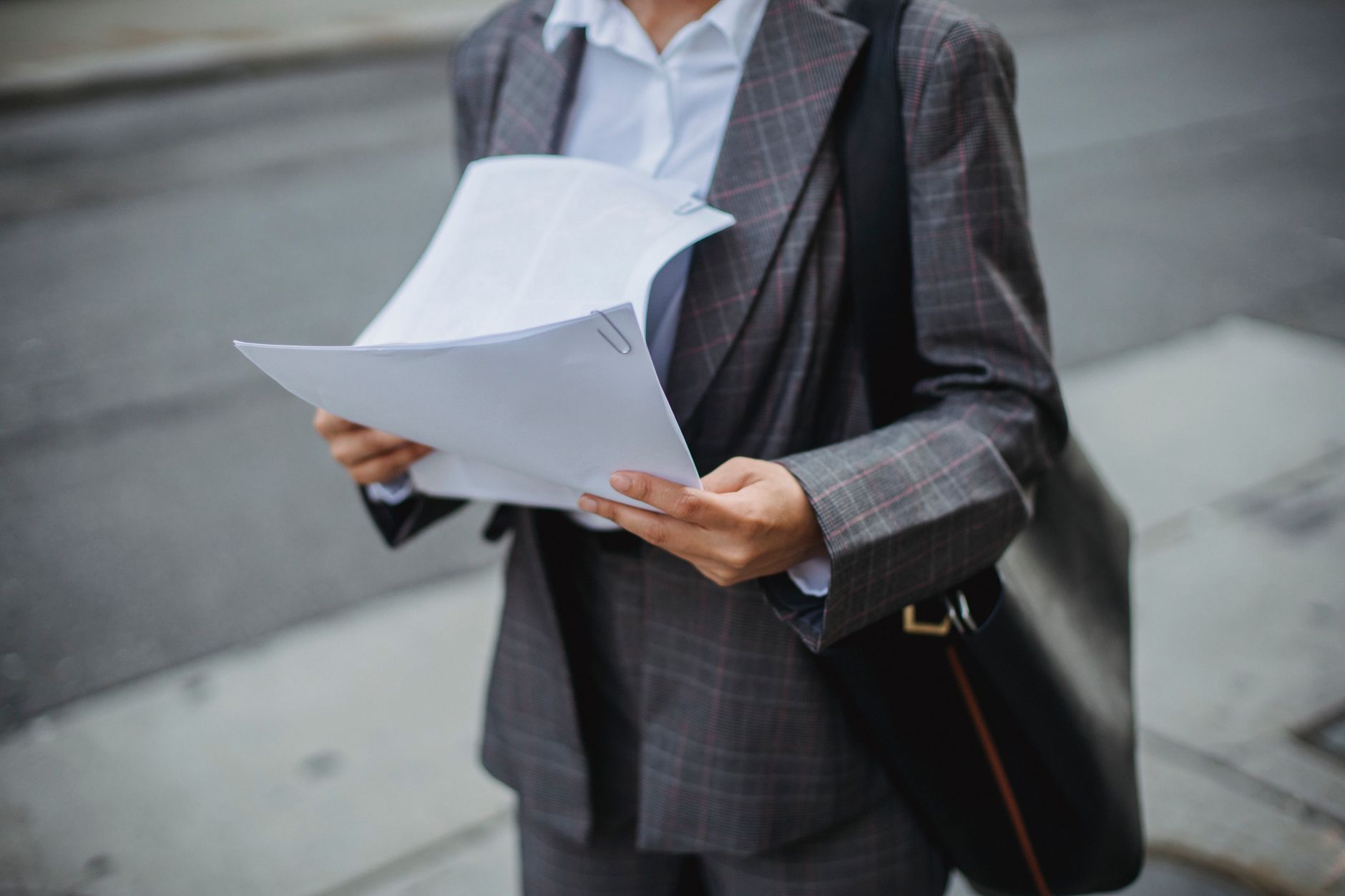 Une personne en costume consulte des feuilles de papier tenues en main dans la rue.